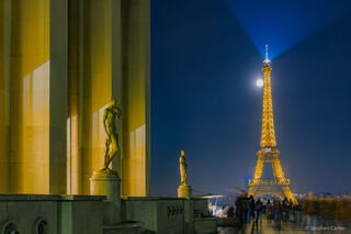 Eiffel Tower at night with a bright full moon rising behind it, viewed from the Palais de Chaillot.